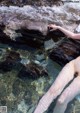 A naked woman laying on a rock in the water.