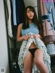 A woman in a blue tank top and black panties sitting on a shelf.