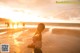 A woman standing on a beach at sunset with people in the background.