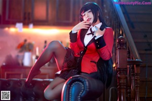 A woman in a red jacket and black skirt sitting on a couch.